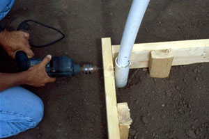Figure 5. Drilling through baseboard, ground post and hoop. Carriage bolts will hold hoop in place.